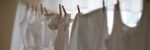 A row of white clothing hangs on a clothesline indoors, softly lit.