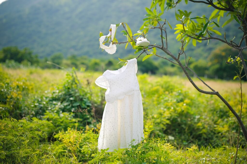 A white baby dress hanging on a tree branch in a lush outdoor setting.